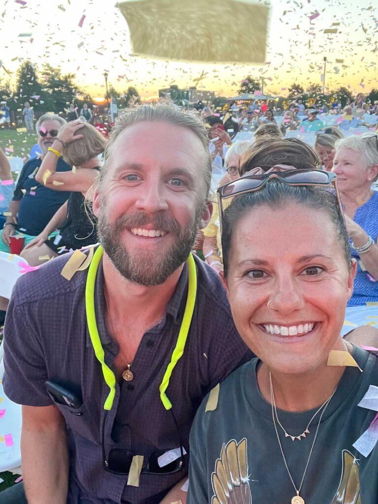 Man and a woman taking a selfie at an outdoor concert with confetti in the air around them.