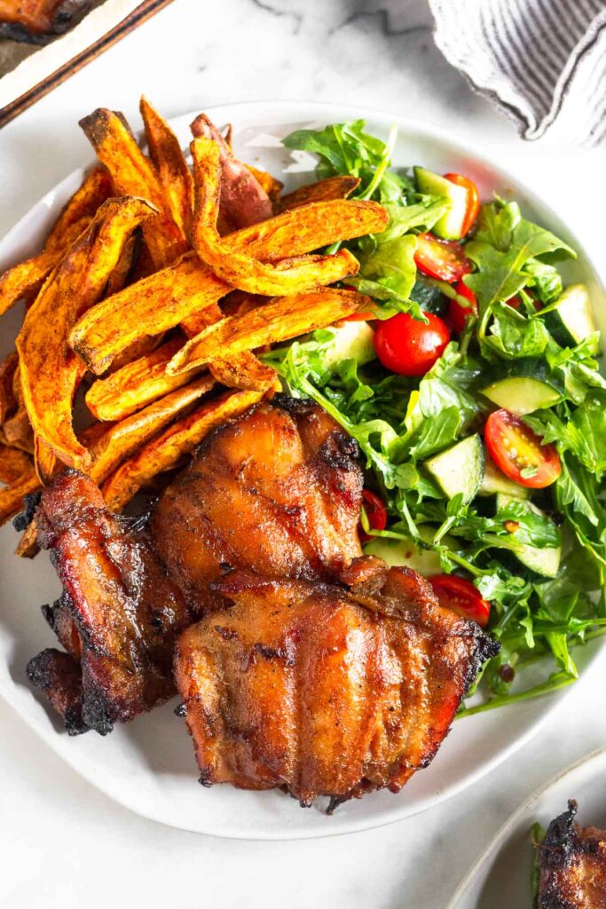 Plate of two grilled chicken thighs, sweet potato fries, and a salad.