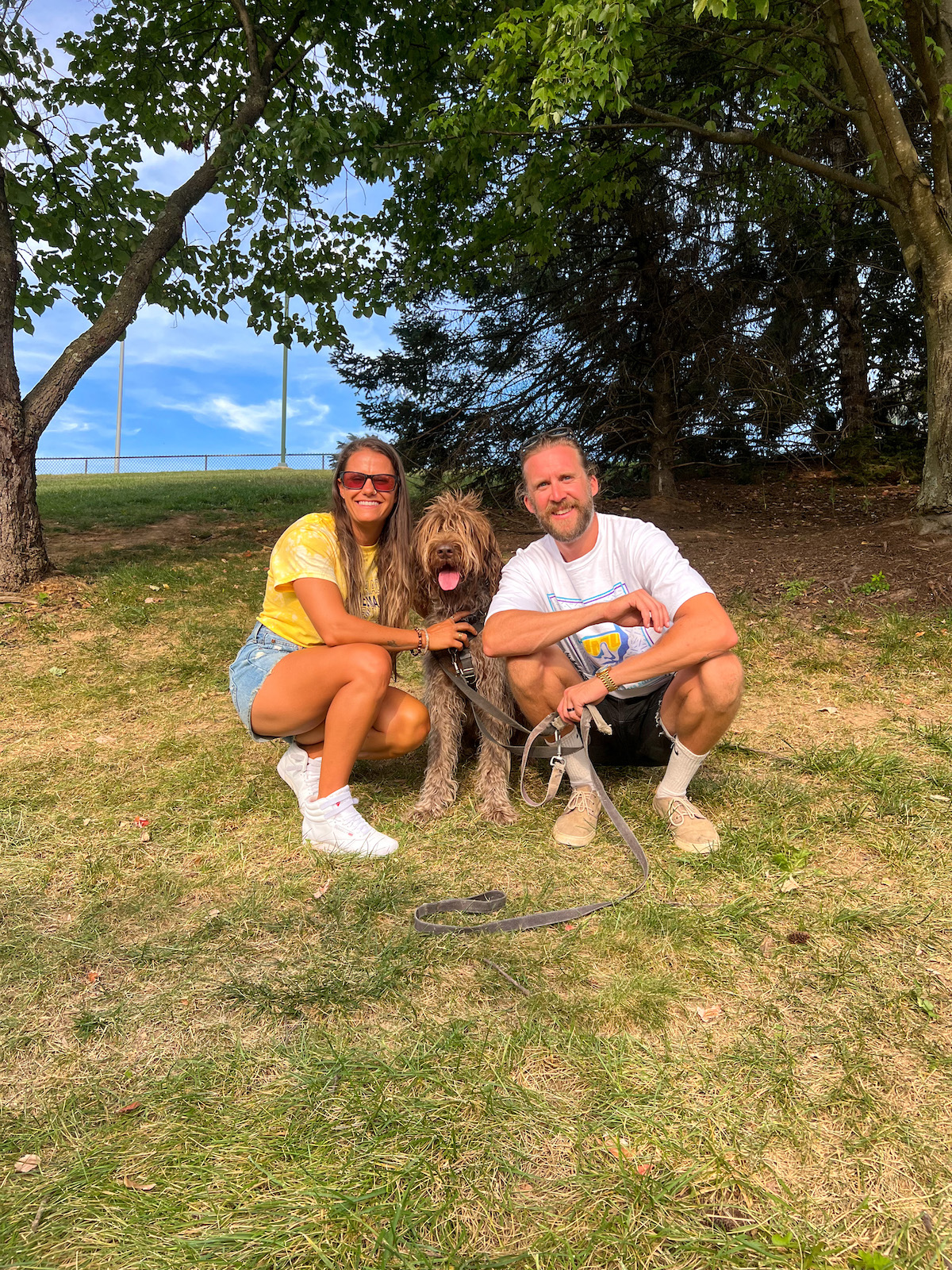 Husband, wife, and their dog sitting on a hill.