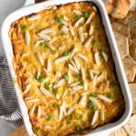 Hot crab dip in a small casserole dish topped with green onions and slivered almonds. Around is it sliced bread and crackers.