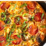 Pizza frittata with pepperoni and veggies in a large white skillet. It is topped with fresh basil and red pepper flakes.
