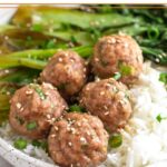 Pork meatballs on top on white rice with sautéed bok choy in a bowl. It is topped with sliced green onions and sesame seeds.