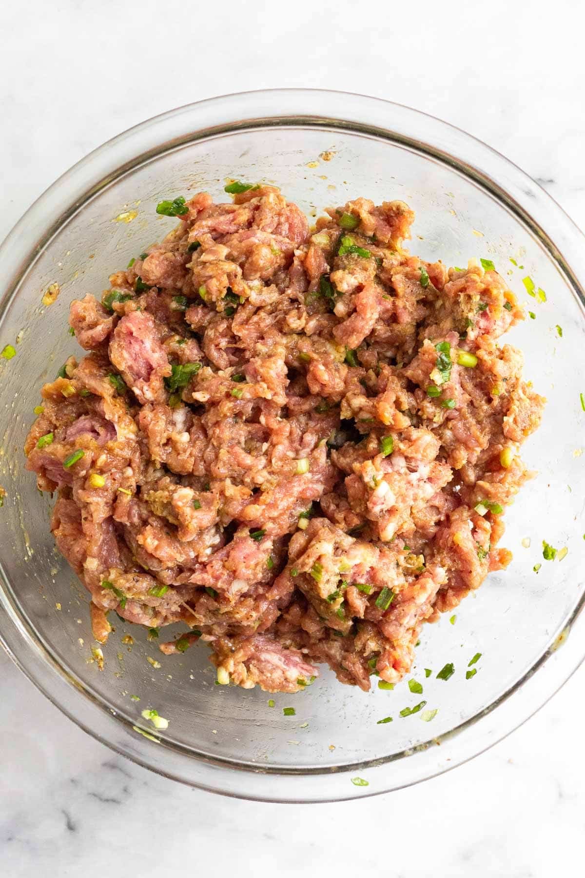 A bowl of ground pork mixed with herbs and spices.