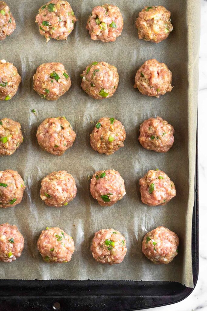 A baking sheet with raw pork meatballs on it.
