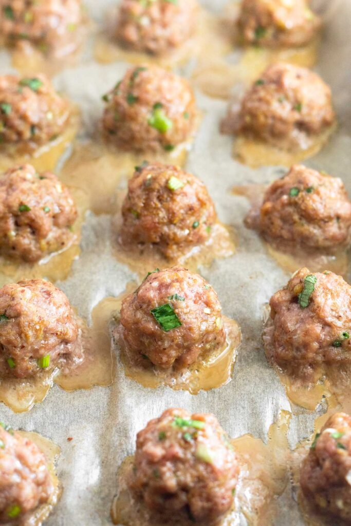 Ground pork meatballs on a baking sheet after they have been baked. A little bit of juice is around each meatball.
