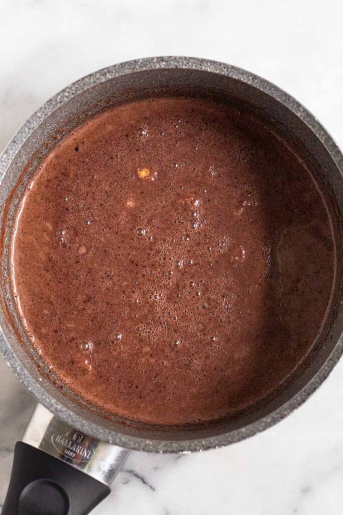 A mixture of milk, cocoa powder, and spices in a small saucepan.