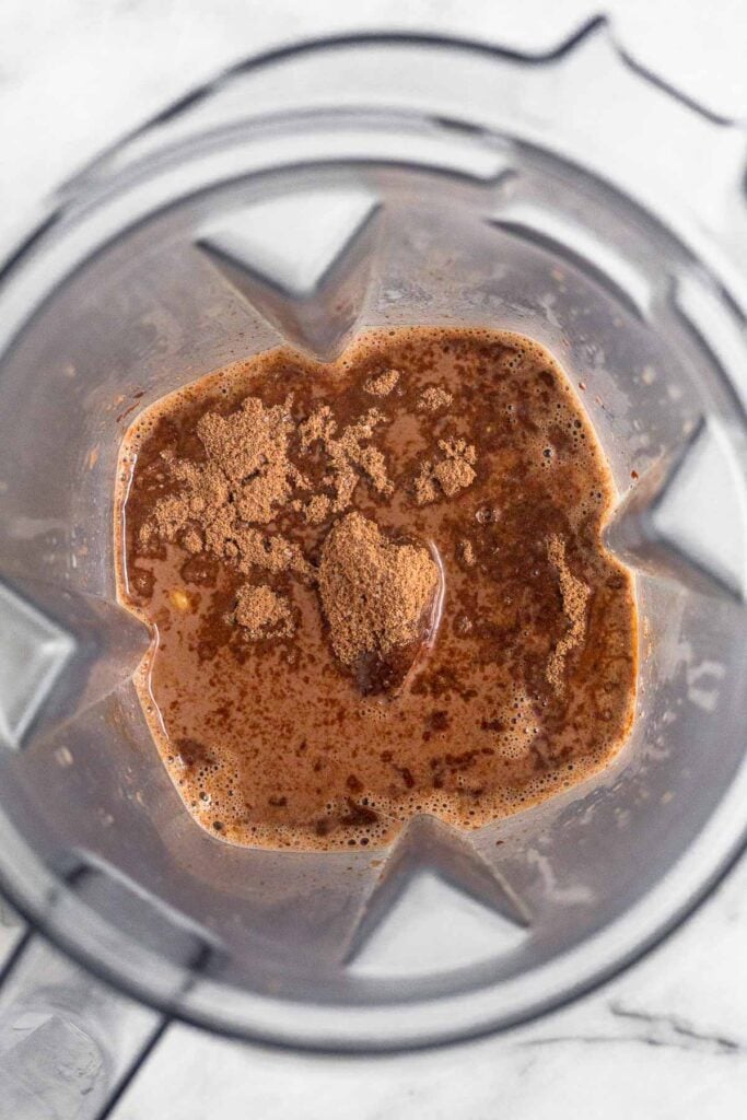 Blender filled with a cocoa powder milk mixture with chocolate protein powder sprinkled on top.