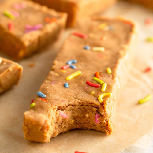 Birthday cake protein bar with a bite taken out of it. Behind it are more protein bars.