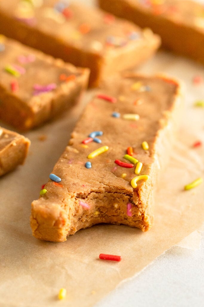 Birthday cake protein bar with a bite taken out of it. Behind it are more protein bars.