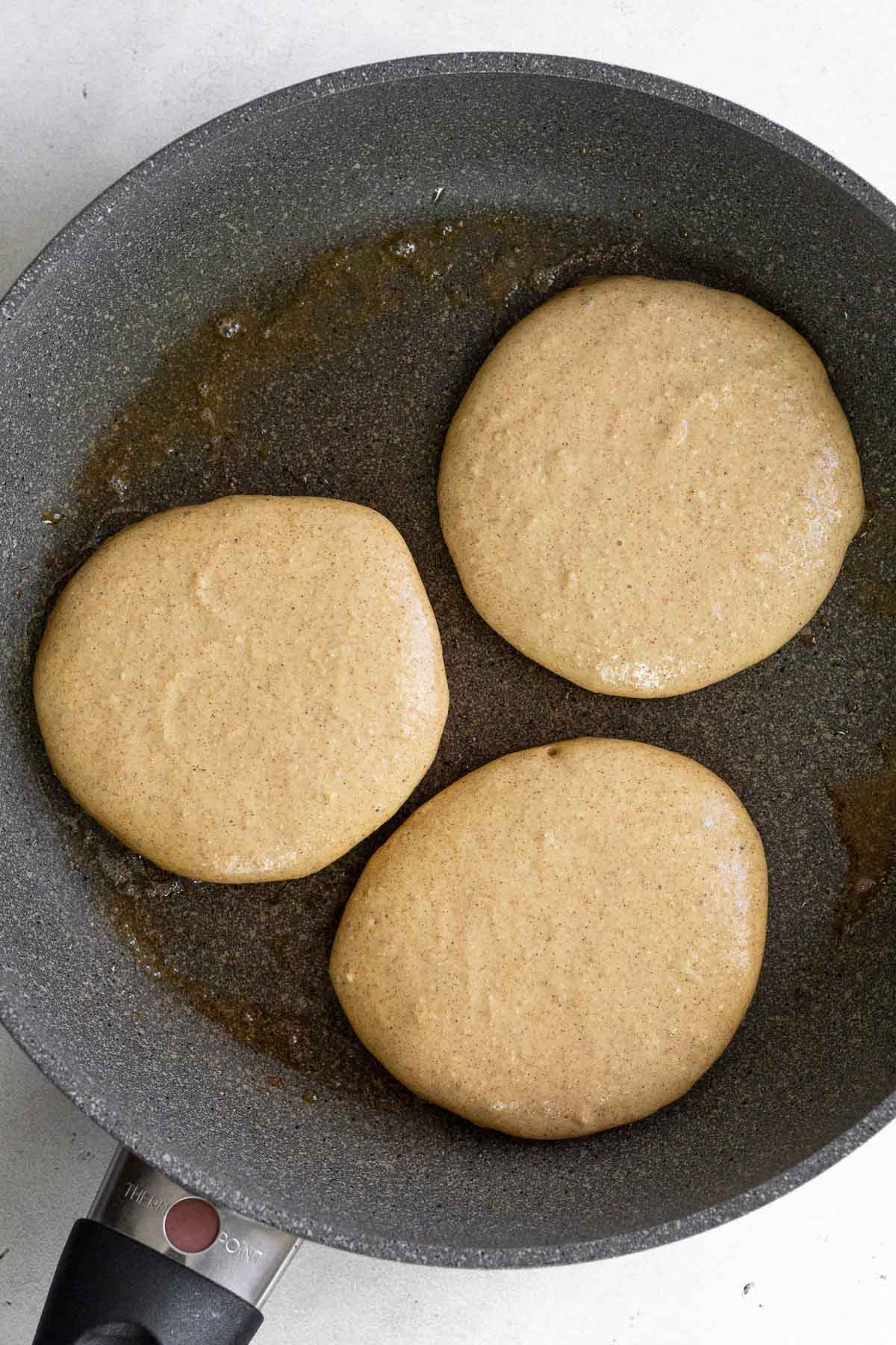 Skillet with 3 pancakes on it before they are flipped.