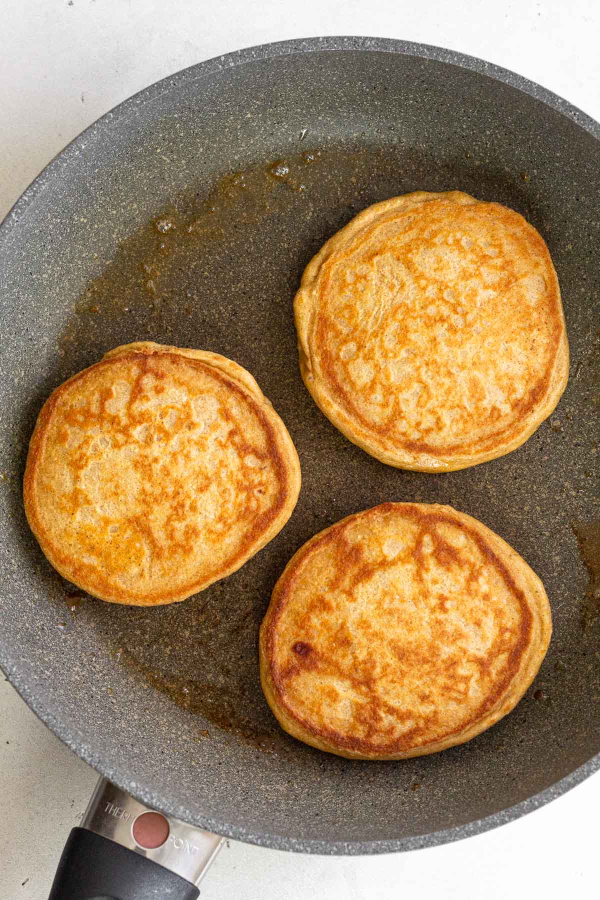 Three pancakes on a grey skillet.