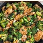 Macro friendly recipe with chicken and broccoli tossed in a brown sauce and garnished with green onions and sesame seeds in a large skillet.