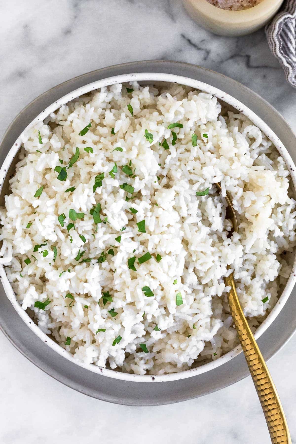 A bowl of coconut rice garnished with cilantro with a spoon in it.