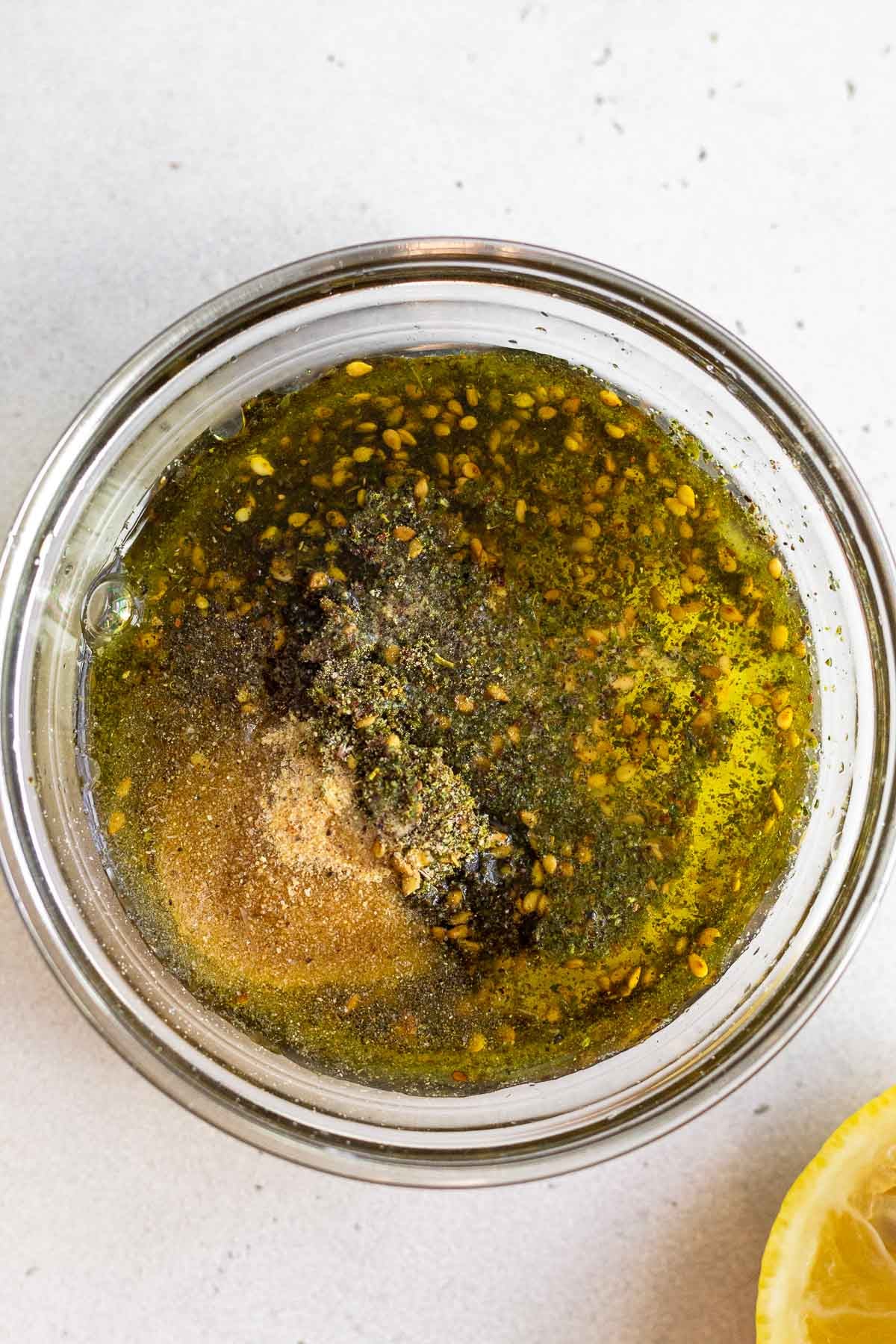 A small glass bowl with olive oil, zaatar, garlic powder, and pepper.