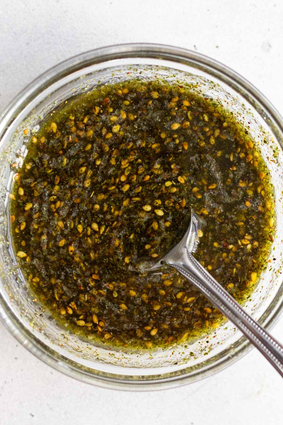 Za'atar marinade in a small glass bowl with a spoon in it.