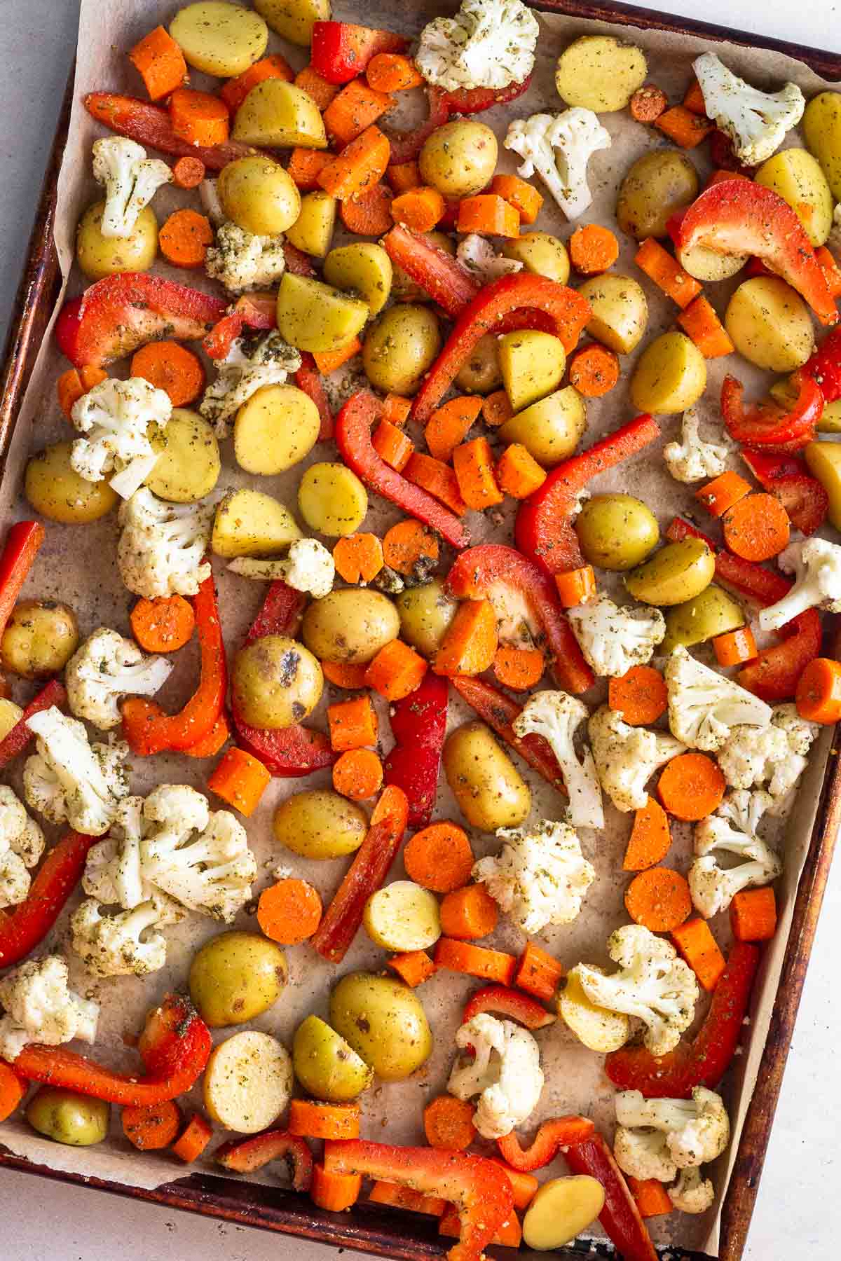 Sheet pan with diced carrots, potatoes, cauliflower, and peppers on it.