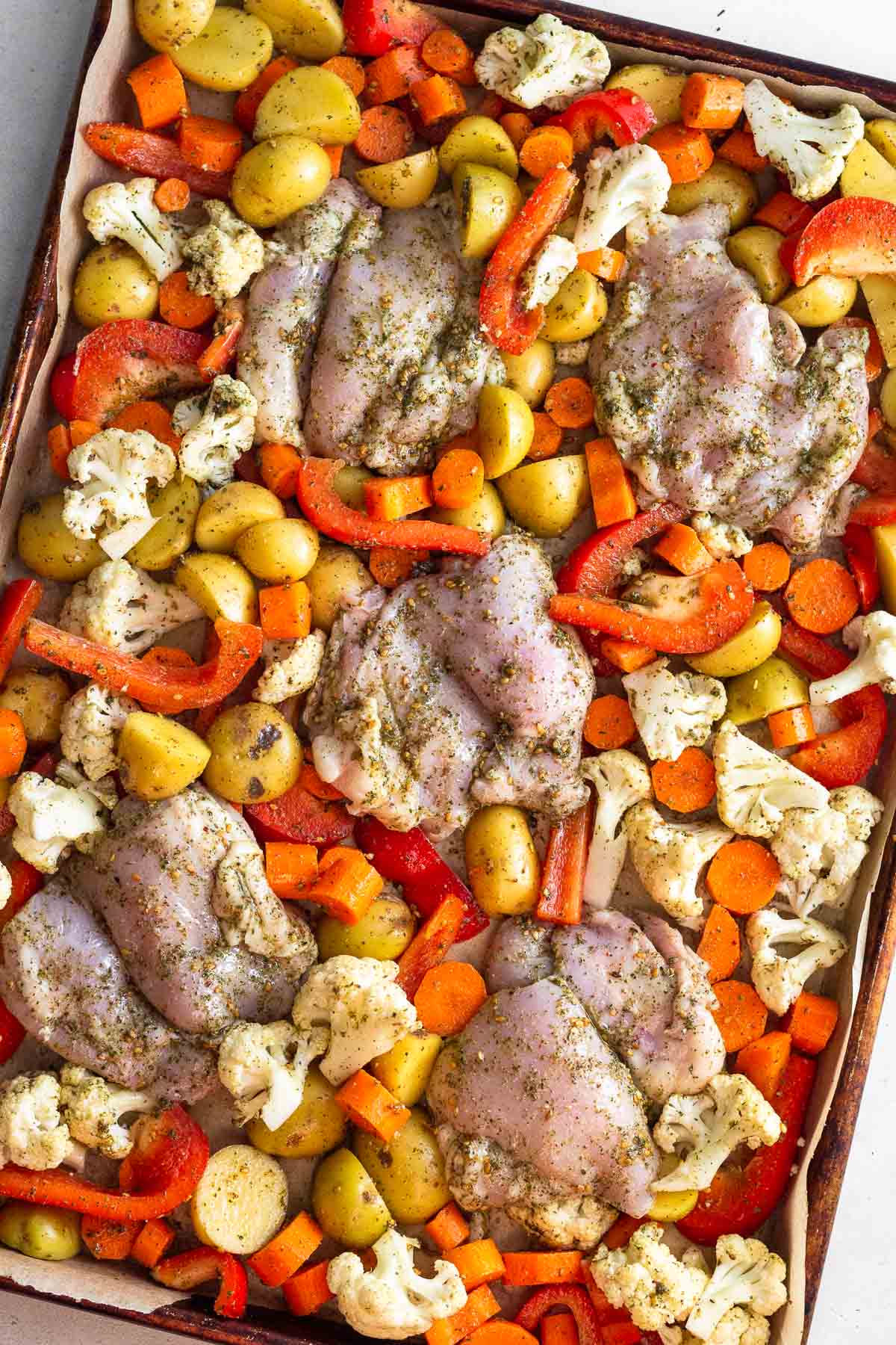 Sheet pan raw chicken thighs, diced carrots, potatoes, cauliflower, and peppers all tossed in zaatar seasoning.