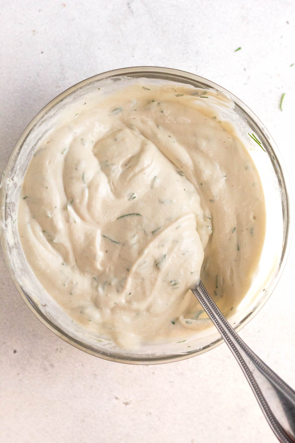 Tahini yogurt sauce in a small glass bowl with a spoon in it.