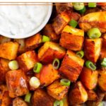 Close up of buffalo potatoes on a plate with a ramekin of blue cheese dressing next to them. They are topped with hot sauce and green onions.