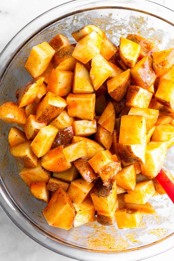 A bowl with diced white potatoes tossed with oil, hot sauce, and spices.
