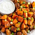 Buffalo potatoes topped with hot sauce and green onions on a plate with a ramekin of blue cheese dressing next to them.
