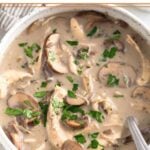 A bowl of creamy chicken mushroom soup topped with fresh parsley. A spoon is in the bowl.