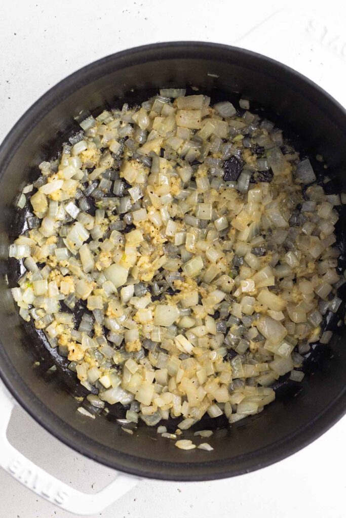 Dutch oven filled with sautéed onions and garlic.