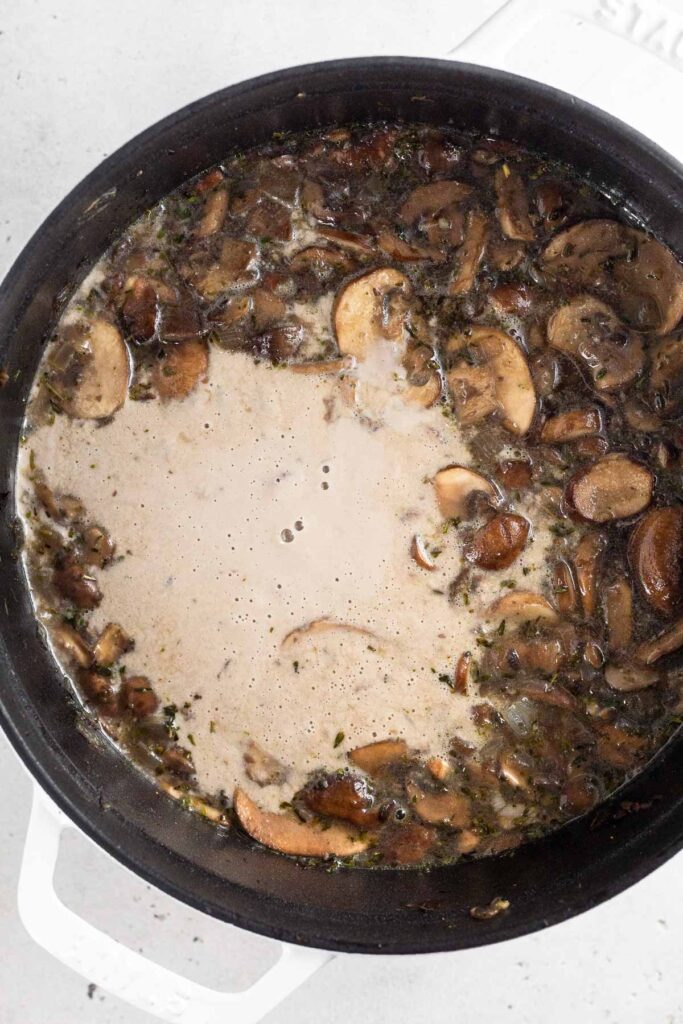 Dutch oven filled with broth, sautéed mushrooms, an a creamy broth that looks like it was just poured in as it has not been mixed together.