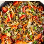 Ground beef and cabbage stir fry in a large cast iron. It is garnished with green onions and sesame seeds.