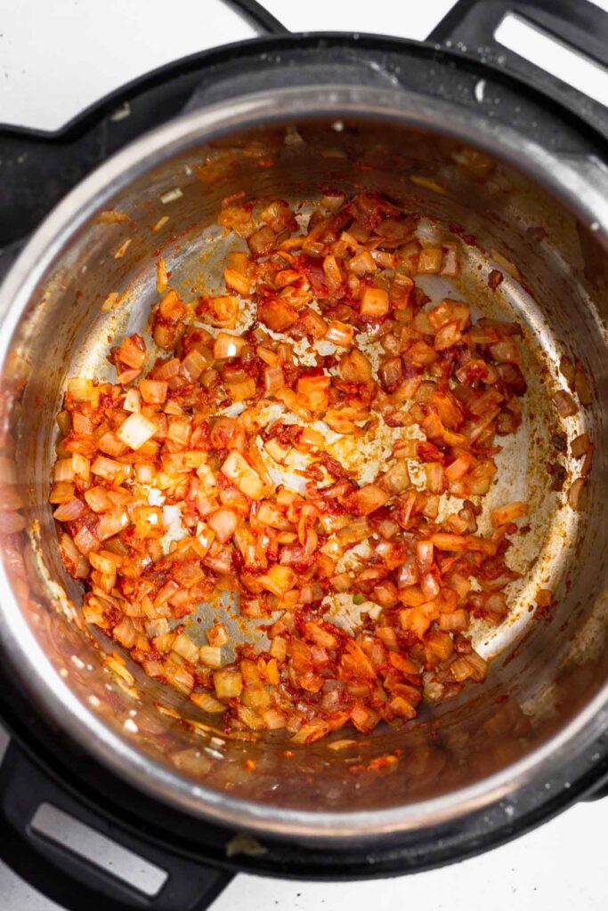Pressure cooker with diced sautéed onions mixed with tomato paste in it.