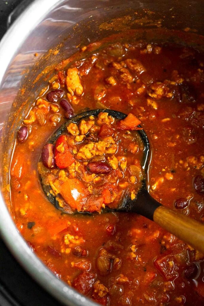 A ladle holding ground turkey chili over a large pot.