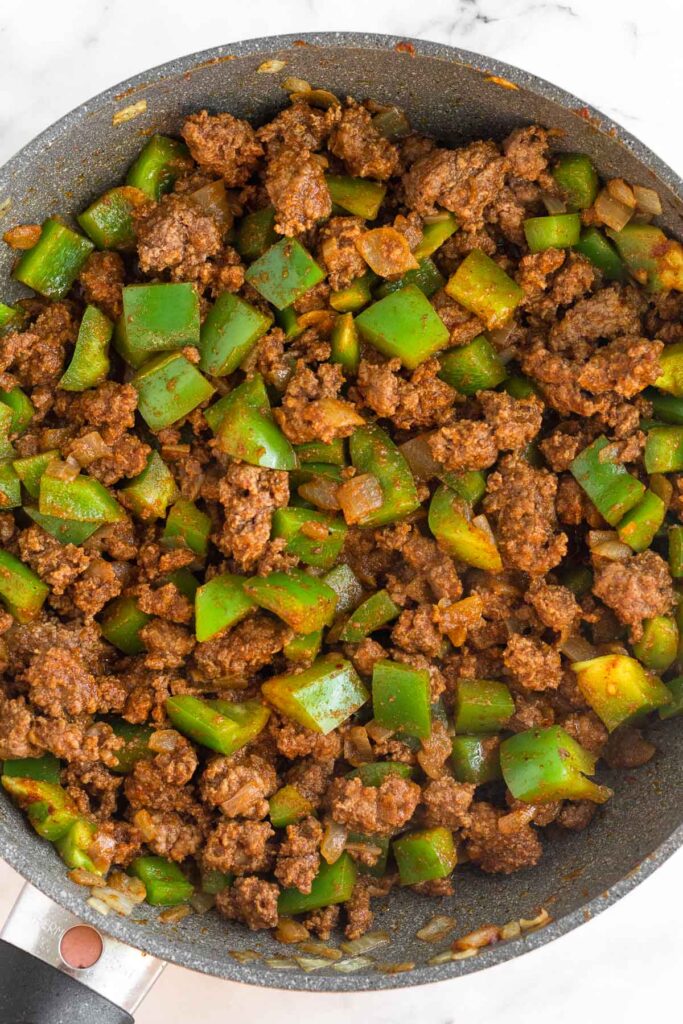 Overhead shot of a skillet filled with sautéed ground beef and diced green peppers.