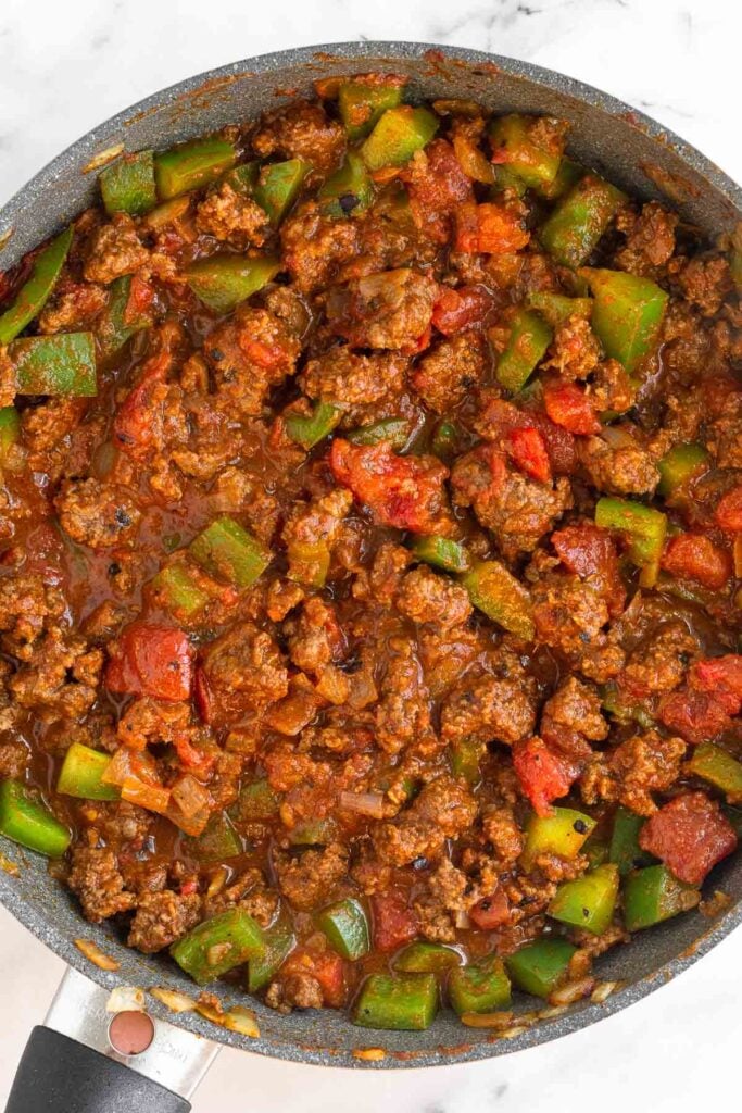 Overhead shot of a skillet filled with sautéed ground beef and diced green peppers mixed with tomato sauce.