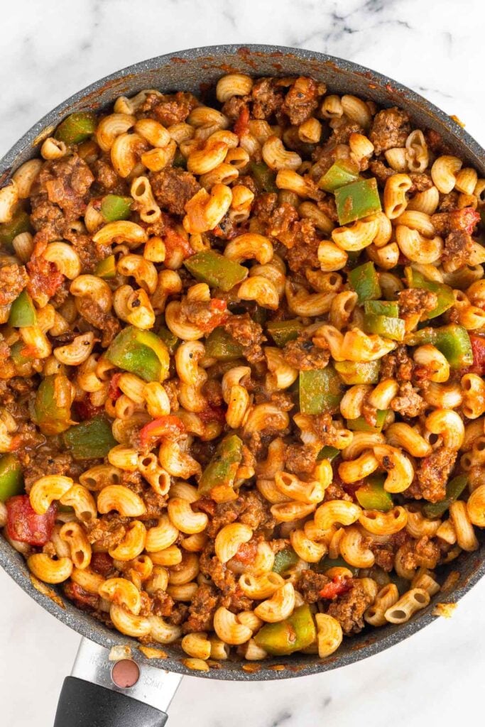 A large skillet filled with cooked elbow macaroni, ground beef, peppers, and diced tomatoes.