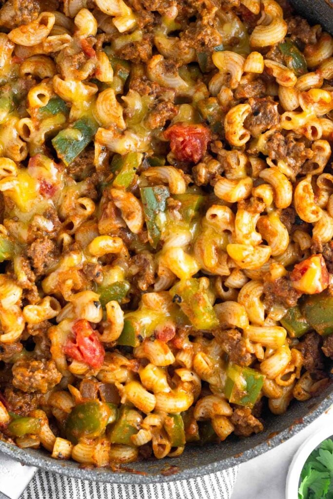 Close up a cheesy beef taco pasta in a large skillet. Next to it is a small ramekin of fresh herbs.