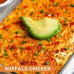 Chicken breakfast casserole in a casserole dish topped with avocado, hot sauce, and green onions. Next to it a ramekin of chopped green onions, ramekin of buffalo sauce, and half an avocado.