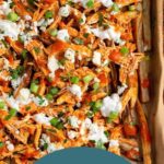 Sheet pan of buffalo chicken fries topped with blue cheese dressing, blue cheese crumbles, green onions, and fresh parsley.