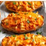 Buffalo chicken stuffed sweet potatoes on a baking sheet drizzled with sauce and topped with fresh herbs.