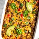 Burrito casserole in a large casserole dish garnished with sliced avocado, sliced jalapeño, and cilantro. Next to it is half an avocado and ramekin of cilantro.
