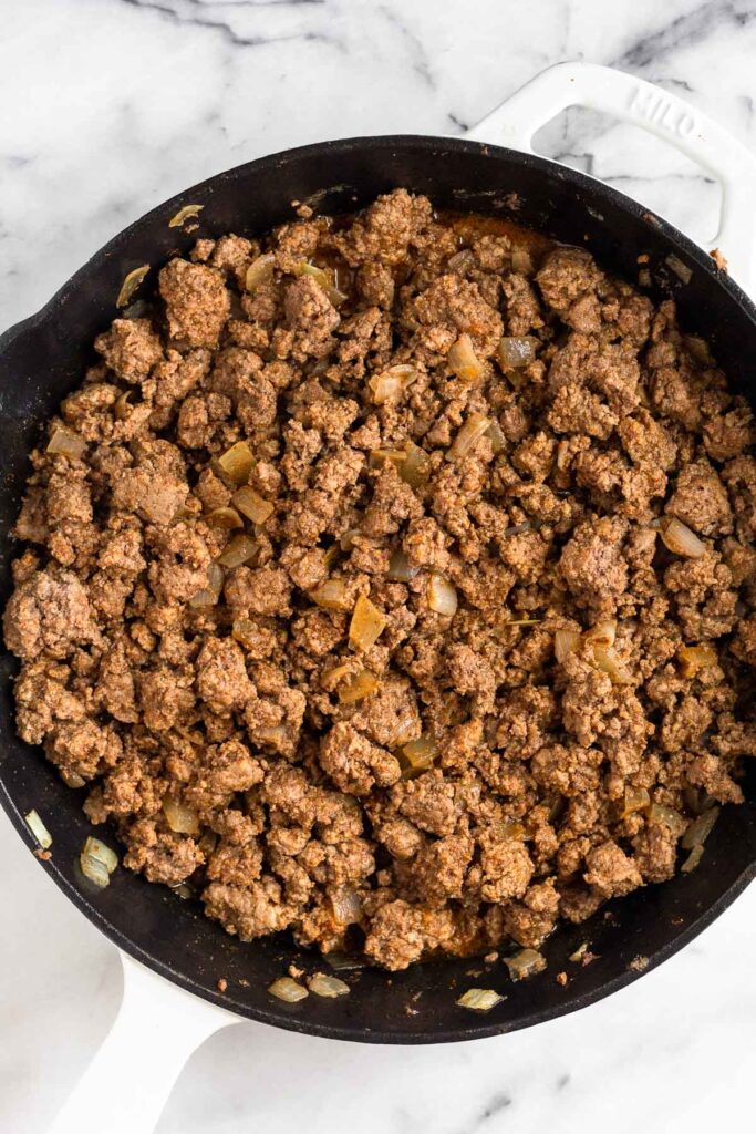 Large cast iron skillet with seasoned ground beef.