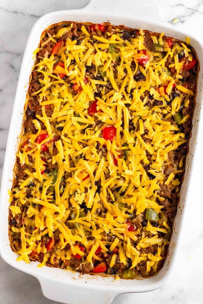 A dish of beef casserole topped with shredded cheese before it is baked.