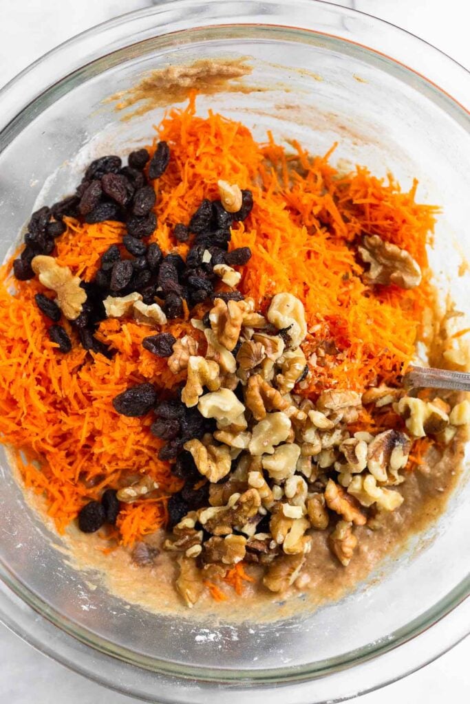 Bowl of cake batter with grated carrots, walnuts, and raisons on top of it before it is mixed it.