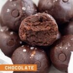 A bowl of healthy chocolate protein balls with chocolate chips and sprinkled with sea salt. The one in the front as a bite taken out of it.