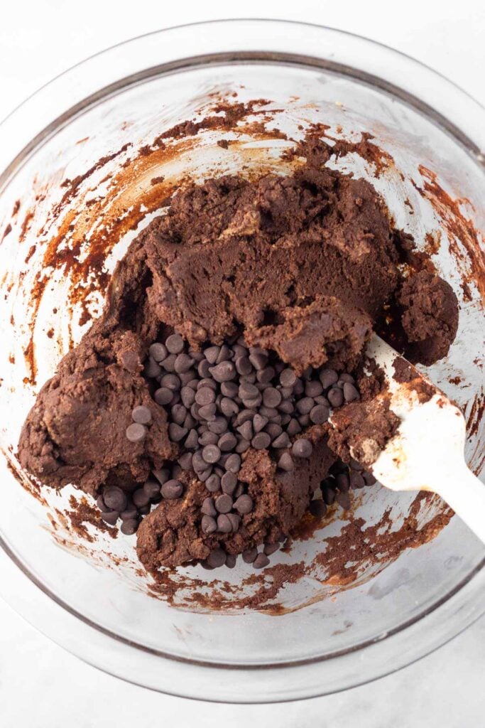 Chocolate batter with chocolate chips sprinkled on top before it is mixed together in a large glass bowl.