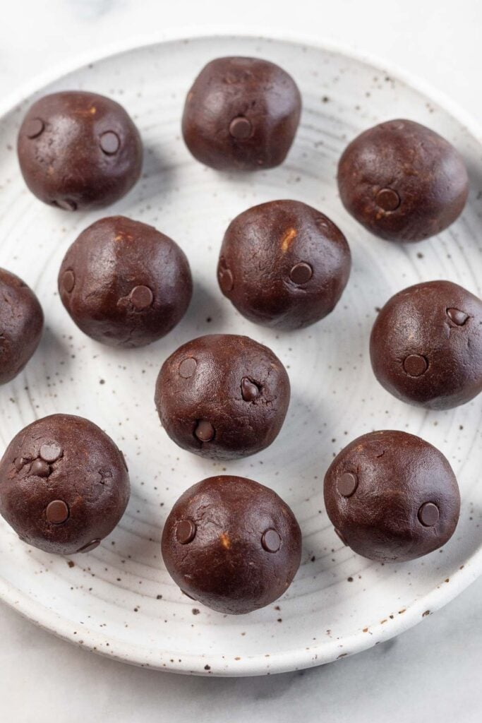 Chocolate chip protein balls spread out on a white plate.