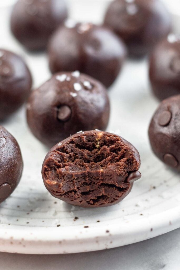 A plate with no bake chocolate protein balls spread out on it. The one in the front as a bite taken out of it.