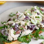 Healthy chicken salad on top of some arugula on a piece of toast on a white plate.