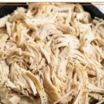 A close-up of a black bowl filled with shredded chicken sprinkled with pepper.