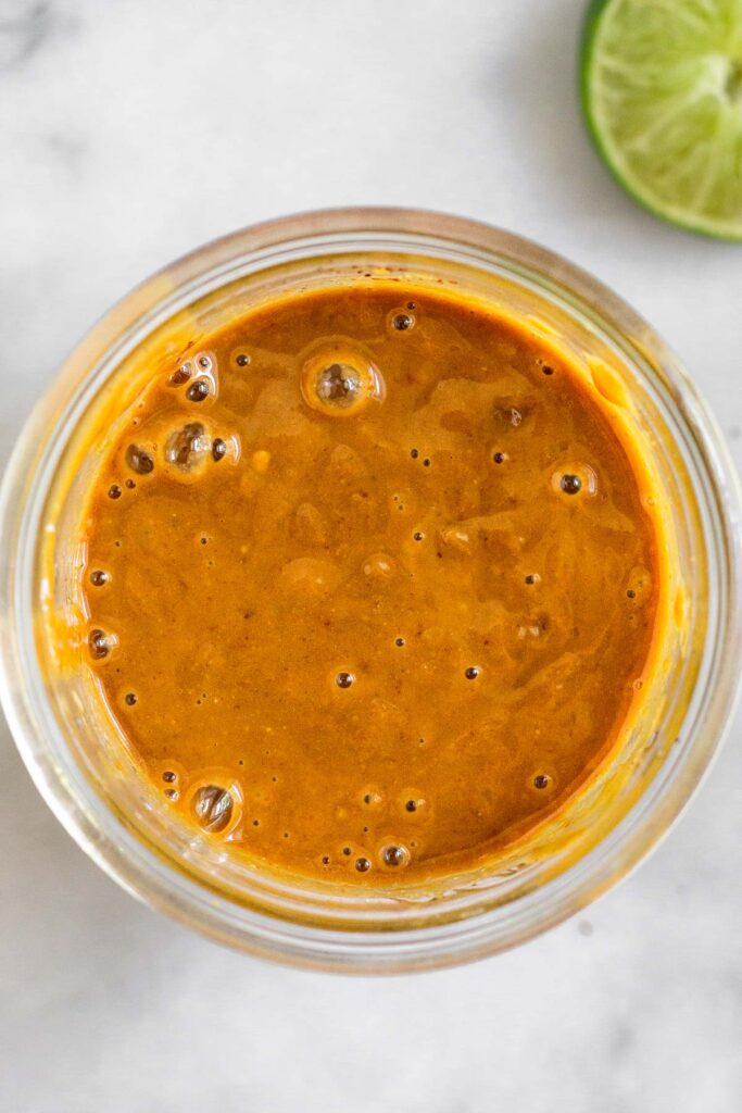 Overhead shot of a jar with Thai peanut sauce in it. Next to it cut a lime.