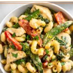 A bowl of tahini pasta with chicken and veggies. It is garnished with fresh herbs and lemon zest.